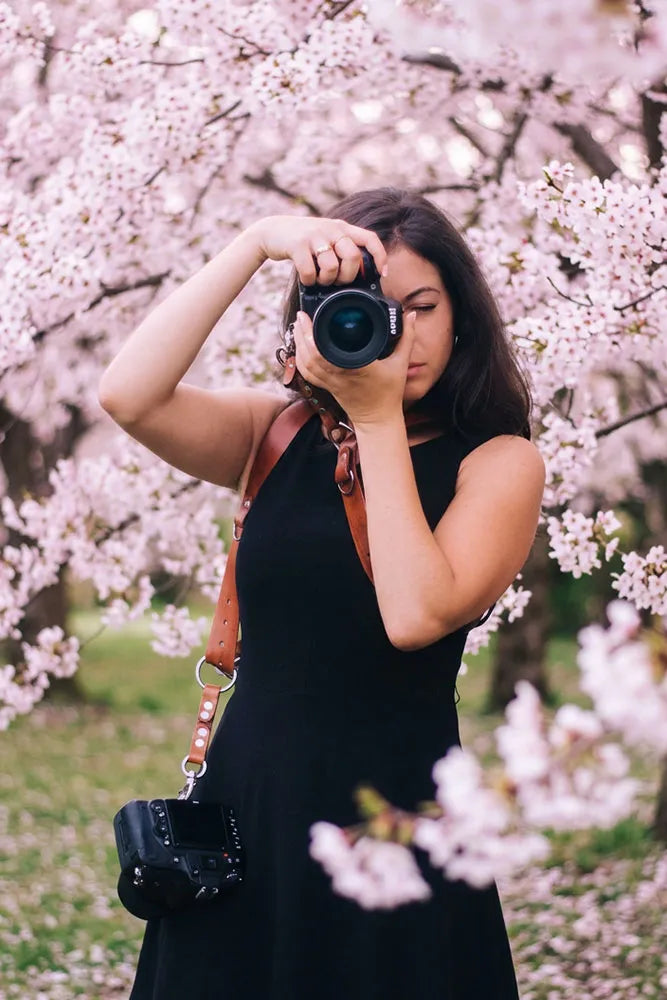 A women with a camera in her hand wearing a leather camera strap with another camera by her side.
