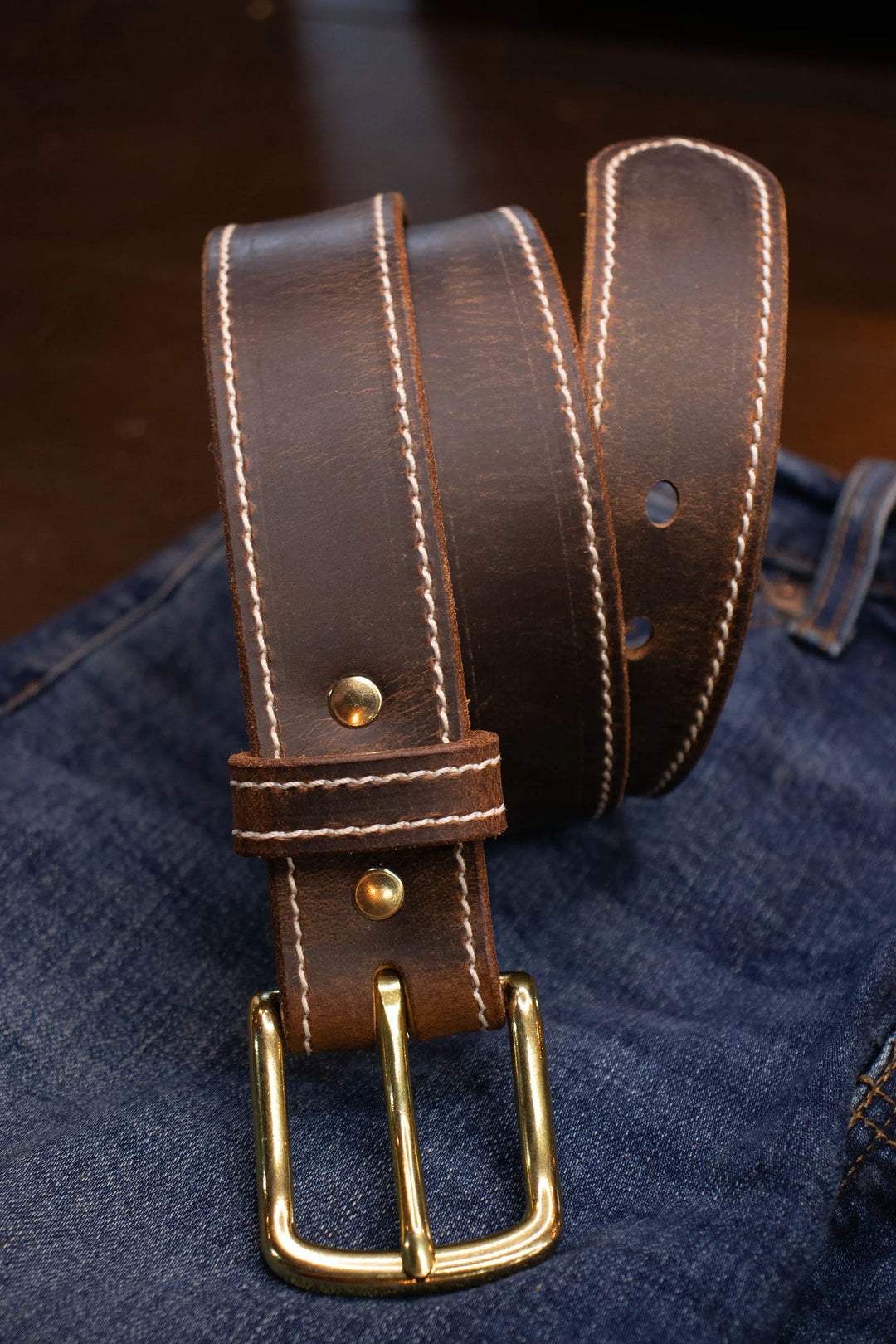 Brown leather belt with brass buckle on a denim background with nice white stitching on belt