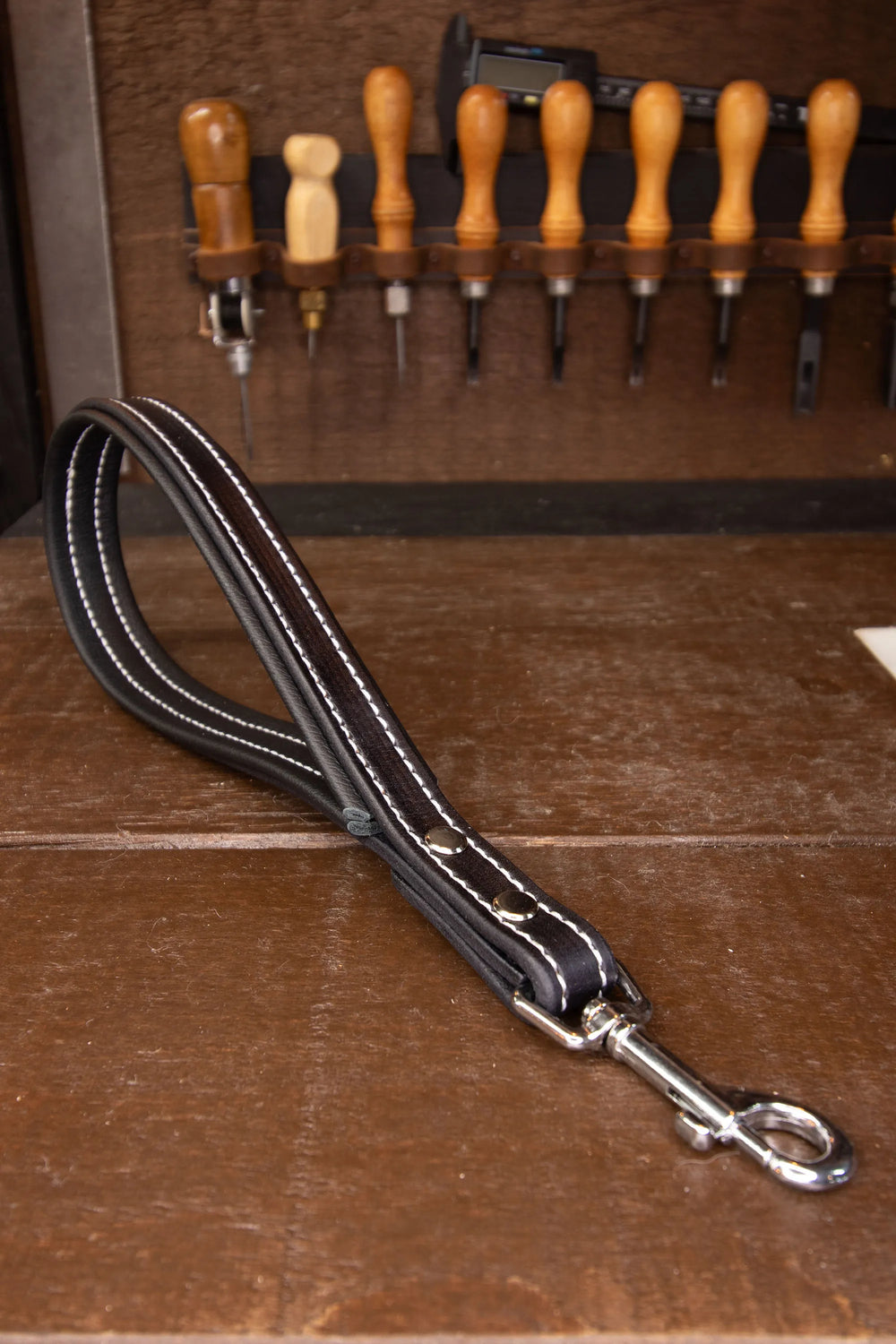 Black leather dog leash with metal clip on a wooden surface with tools in the background
