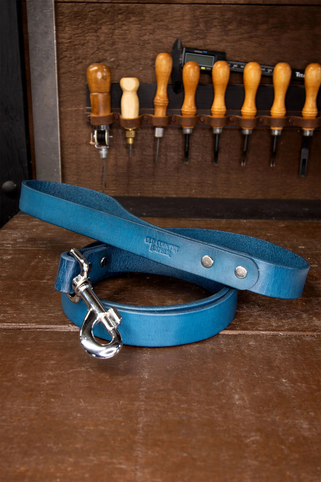 Blue leather dog leash with silver clasp on a wooden surface with tools in the background