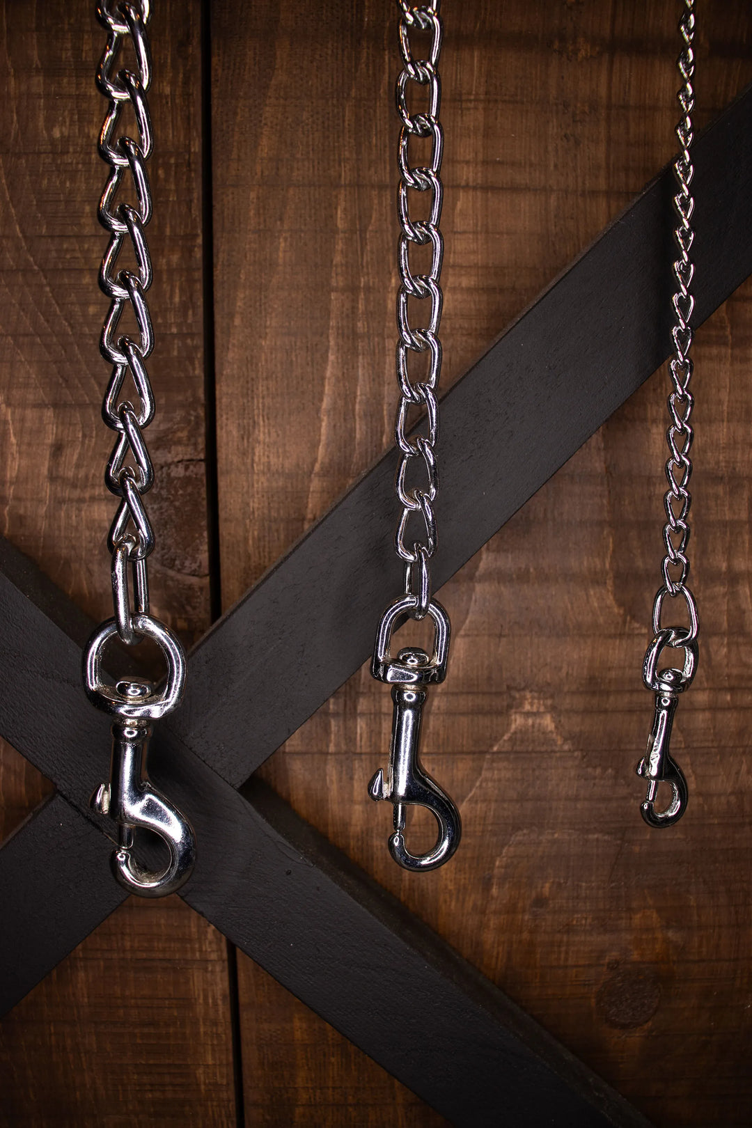 3 chains showing different thicknesses handing in front of a wooden cabinet
