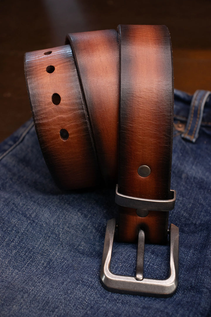 Brown leather belt dyed with multiple colors creating a burnt look with antique nickel buckle and loop keeper on a denim background