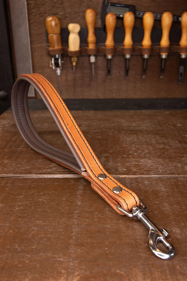 Brown leather dog leash with metal clip on a wooden surface with tools in the background