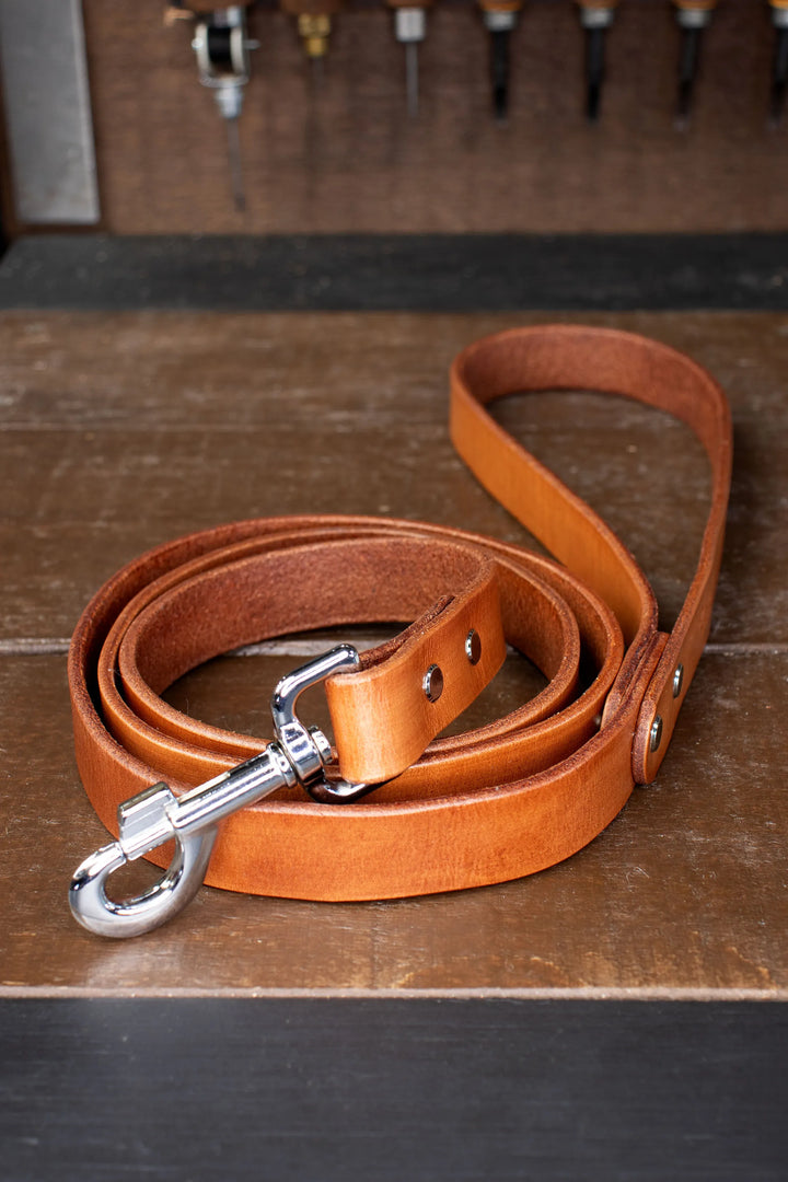 Tan leather dog leash with silver clip on a wooden surface