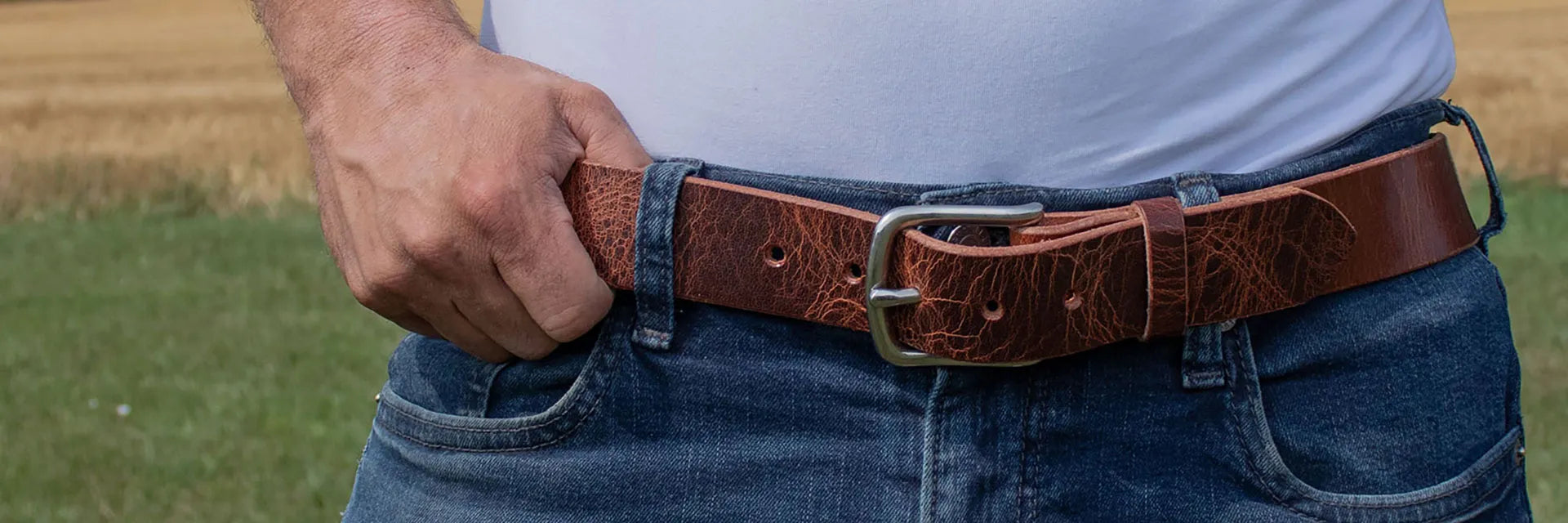Person wearing a brown leather belt with a textured pattern, standing in a field.