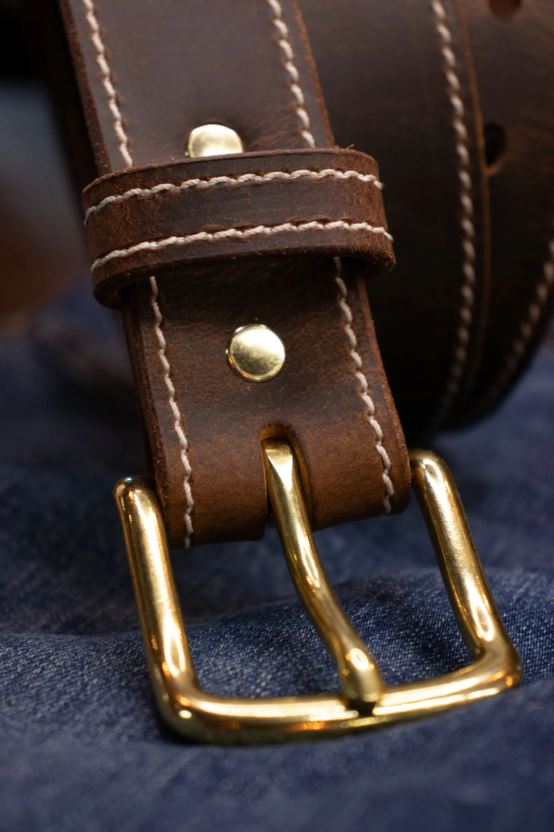 Close-up of a brown leather belt with a gold buckle on a dark fabric background