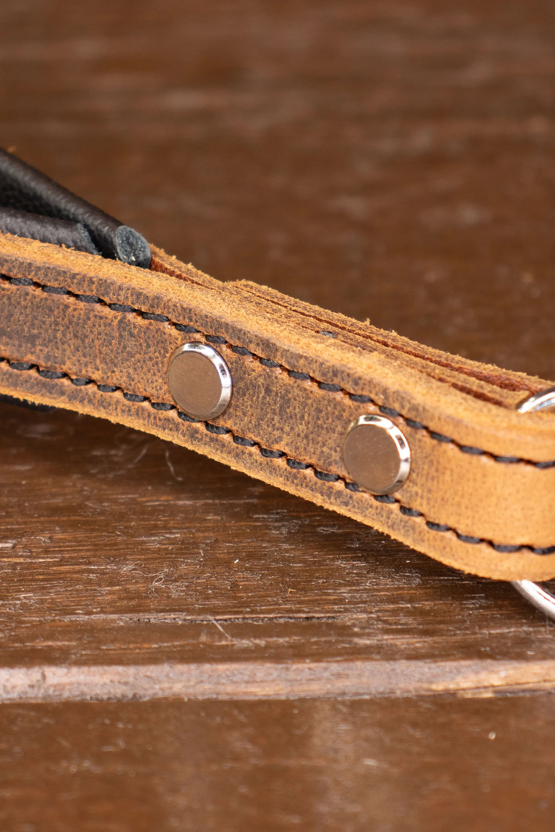 Close-up of a brown leather strap with metal chicago screws on a wooden surface
