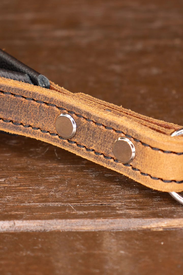 Close-up of a brown leather strap with metal chicago screws on a wooden surface