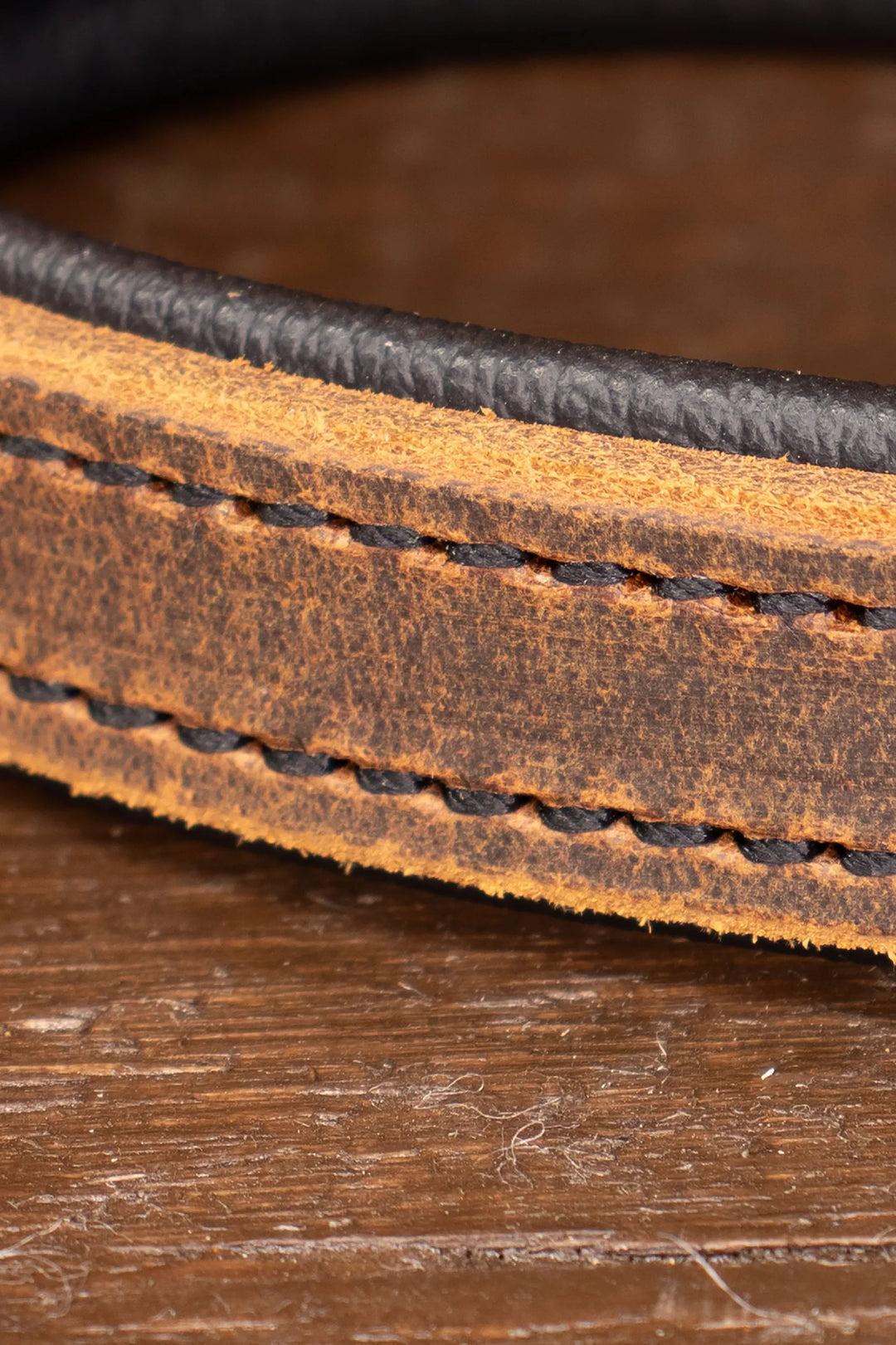 Close-up of a brown leather leash handle with heavy duty stitching on a wooden surface