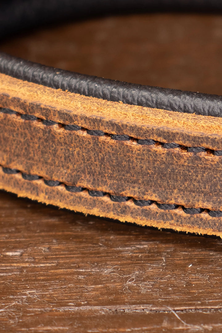 Close-up of a brown leather leash handle with heavy duty stitching on a wooden surface